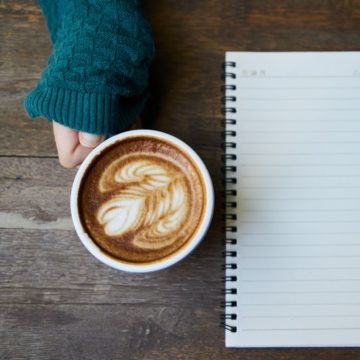 Coffe cup, notebook, person's hand and sleeve