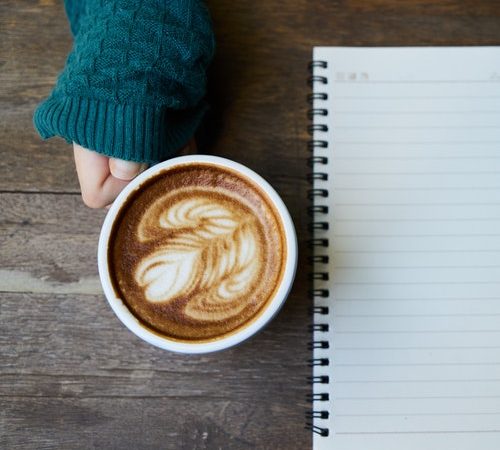 Coffe cup, notebook, person's hand and sleeve